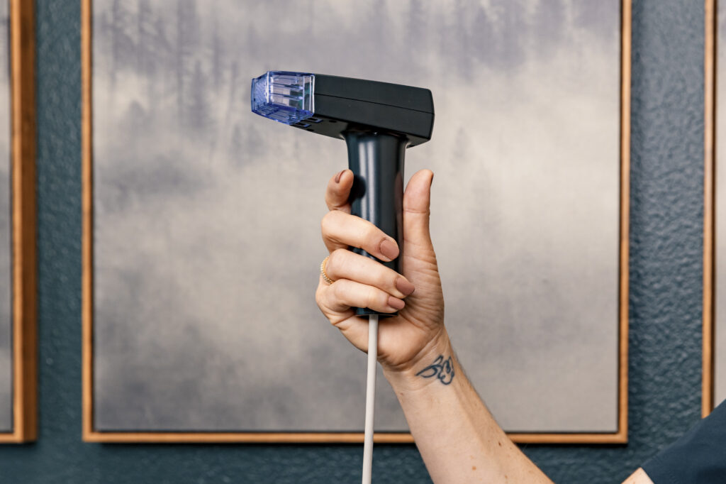 A provider's arm holds up our handheld device for Morpheus8 in Reno, a foggy alpine image in the background.