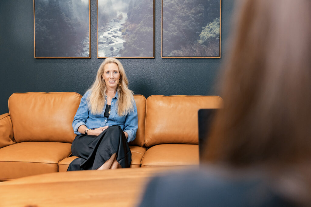 A blonde woman sits on a leather couch in our office for her first consultation, where she speaks with a provider about family medicine in Reno.