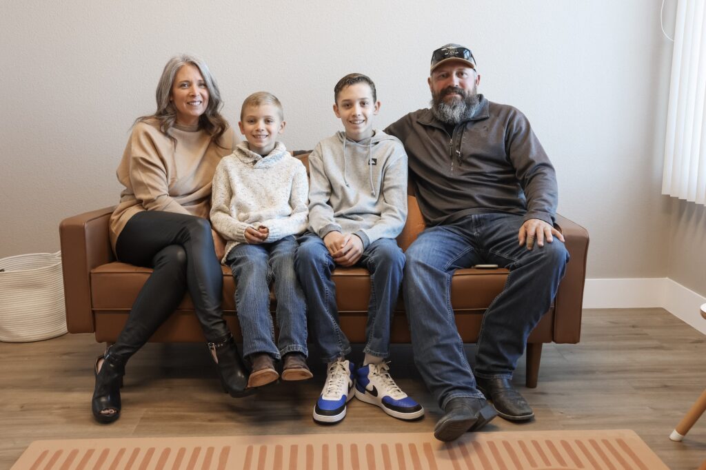 A family of a mom, dad, and two sons, sit on a couch ready for concierge primary care in Reno.